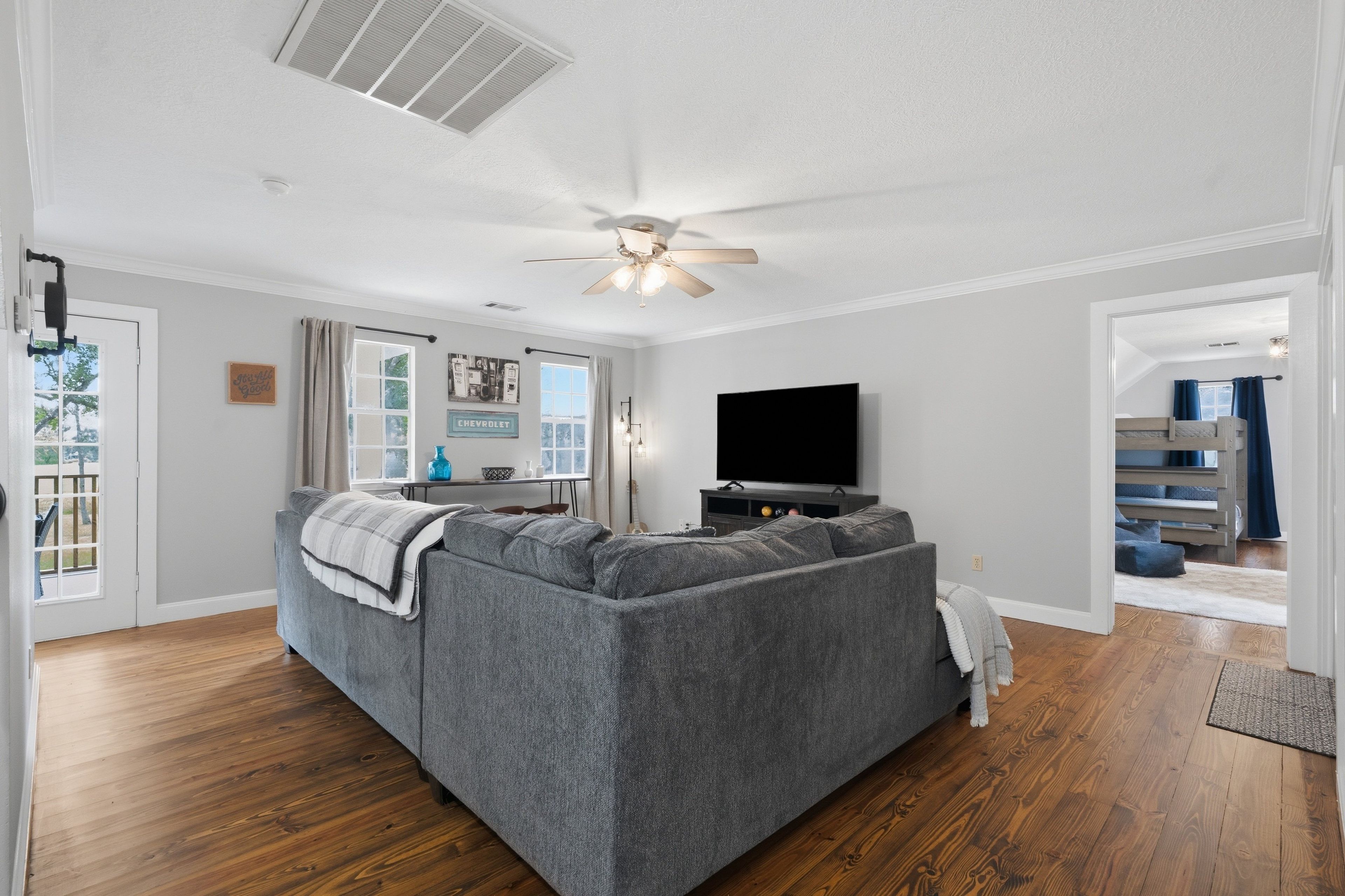 A modern living room with a gray sectional sofa, a flat-screen TV, and a ceiling fan.
