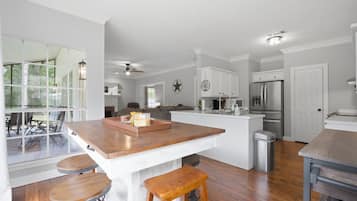 A modern kitchen with a central island, wooden stools, and a view through large windows.