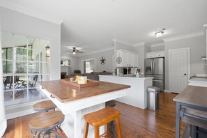 A modern kitchen with a central island, wooden stools, and a view through large windows. - Country Living Near Lake Houston - Starry Skies 3 Bedroom Home (Dayton)