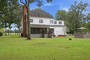 A two-story house with a large front porch, a brick chimney, and a fenced yard. - Country Living Near Lake Houston - Starry Skies 3 Bedroom Home (Dayton)