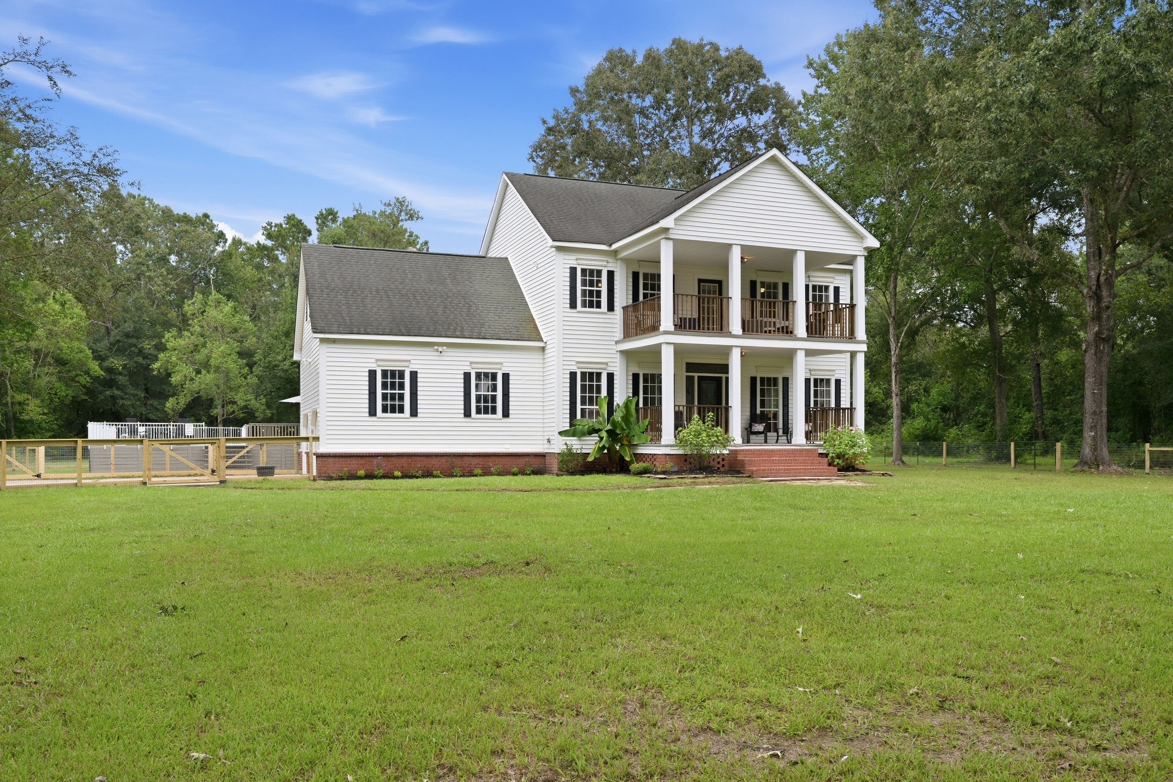 A two-story house with a front porch, a fenced yard, and a large tree to the right.