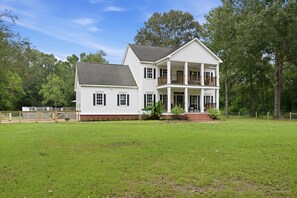 A two-story house with a front porch, a fenced yard, and a large tree to the right. - Country Living Near Lake Houston - Starry Skies 3 Bedroom Home (Dayton)