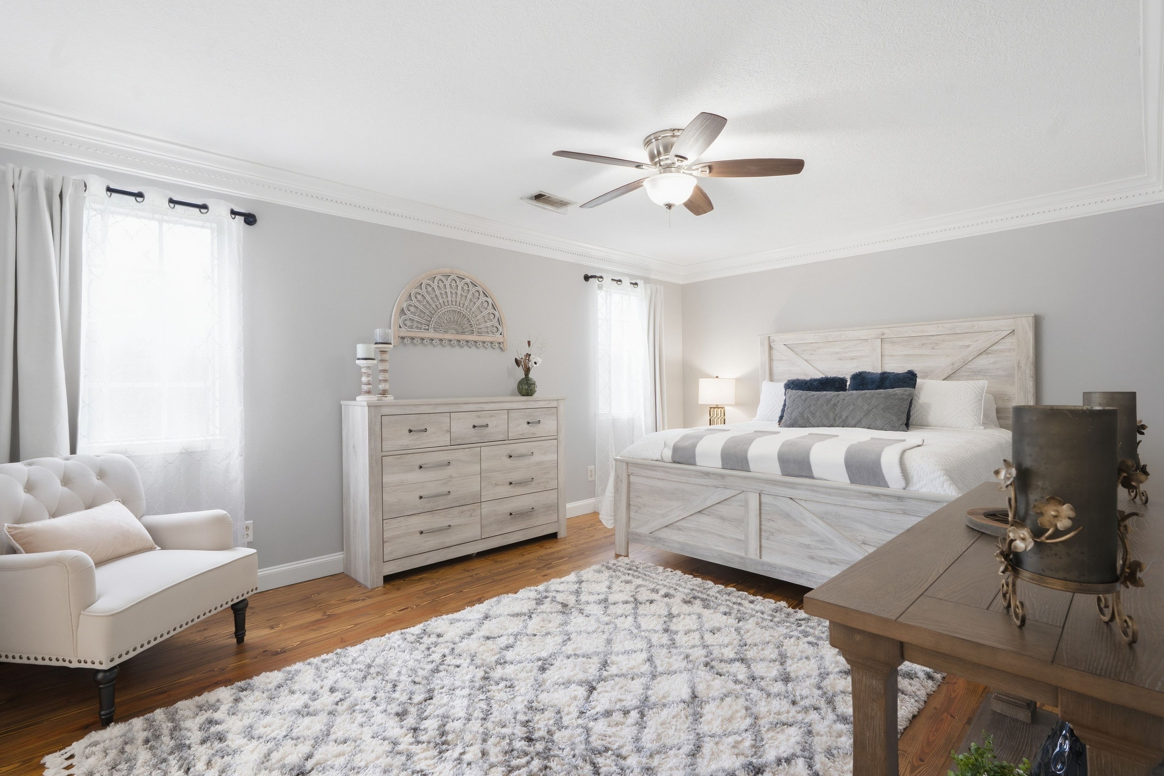 A bedroom with a bed, dresser, chair, and a ceiling fan.