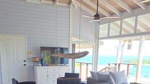 Uma sala de jantar com mesa e cadeiras de madeira, cozinha com armário branco e vista para o oceano.