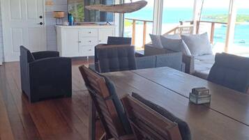 A dining area with a wooden table and chairs, a kitchen area with a white cabinet, and a view of the ocean.