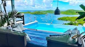 Uma área de estar junto à piscina, com vista para uma marina e vegetação.