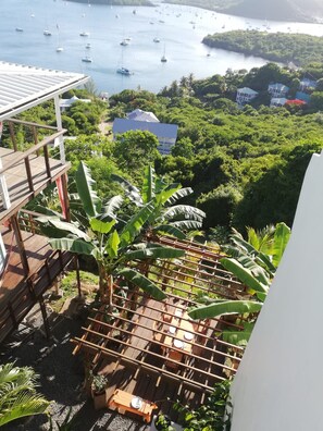Un balcón con vista a una bahía con barcos, rodeado de exuberante vegetación y una casa.
