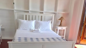 Cama branca com tapete listrado em frente, luminária de cabeceira e ar-condicionado fixado na parede.