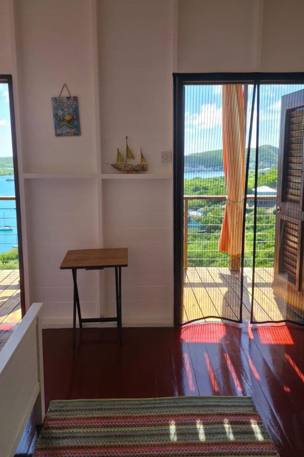 A room with a wooden table, a colorful rug, a view of the outdoors through a sliding door, and a shelf with decorative items.
