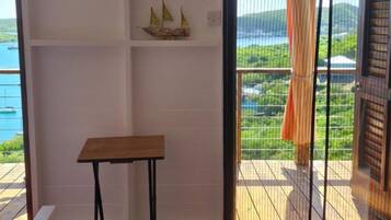A room with a wooden table, a colorful rug, a view of the outdoors through a sliding door, and a shelf with decorative items.