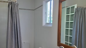Casa de banho com lavatório branco, espelho, sanita e cortina de chuveiro.