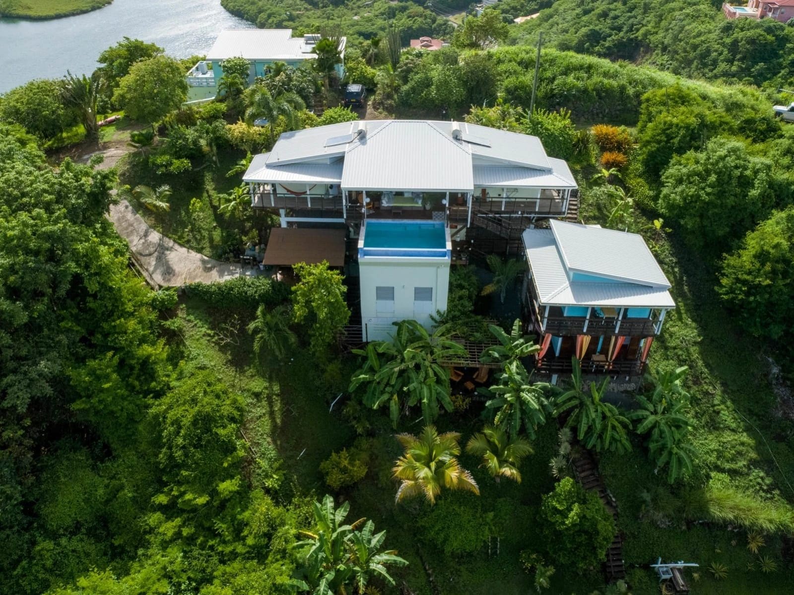 A large, multi-story house surrounded by dense tropical vegetation, with a prominent blue-roofed structure in the center.