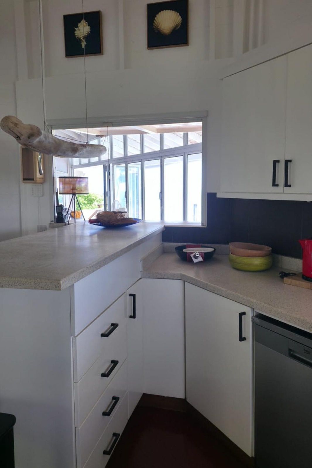 A kitchen with white cabinets, a large window, and a countertop with various kitchen items.