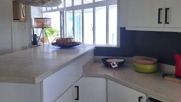 A kitchen with white cabinets, a large window, and a countertop with various kitchen items.