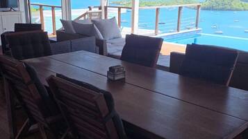 Un comedor con una mesa grande y sillas, un ventilador de techo y vista al océano.