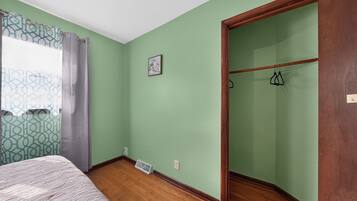 Une pièce avec un lit, une fenêtre ornée de rideaux à motifs, un tableau accroché au mur et une armoire en bois.