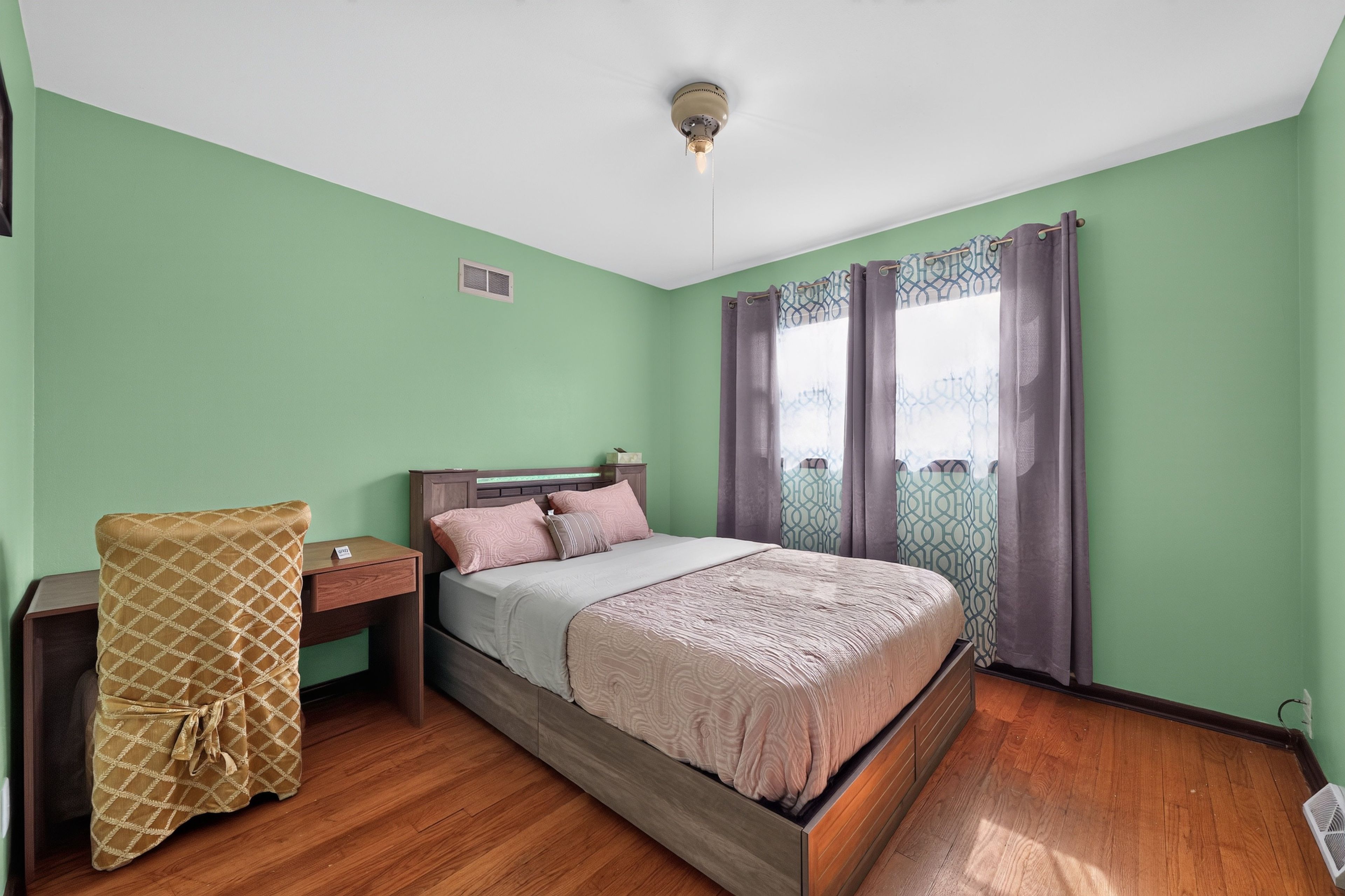 A bedroom with a bed, a nightstand, a chair, and a window with curtains.