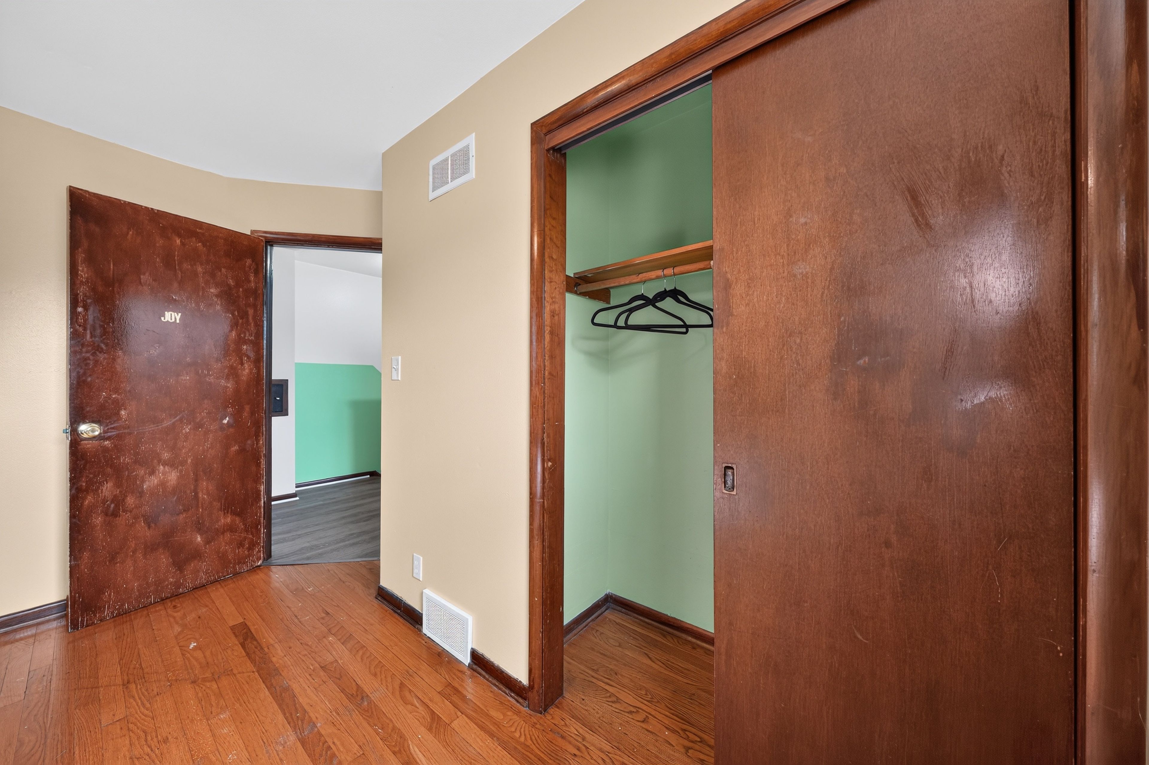 Un pasillo con suelo de madera, un armario con perchas y una puerta que da a otra habitación.