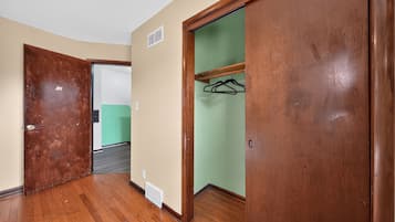 Un pasillo con suelo de madera, un armario con perchas y una puerta que da a otra habitación.
