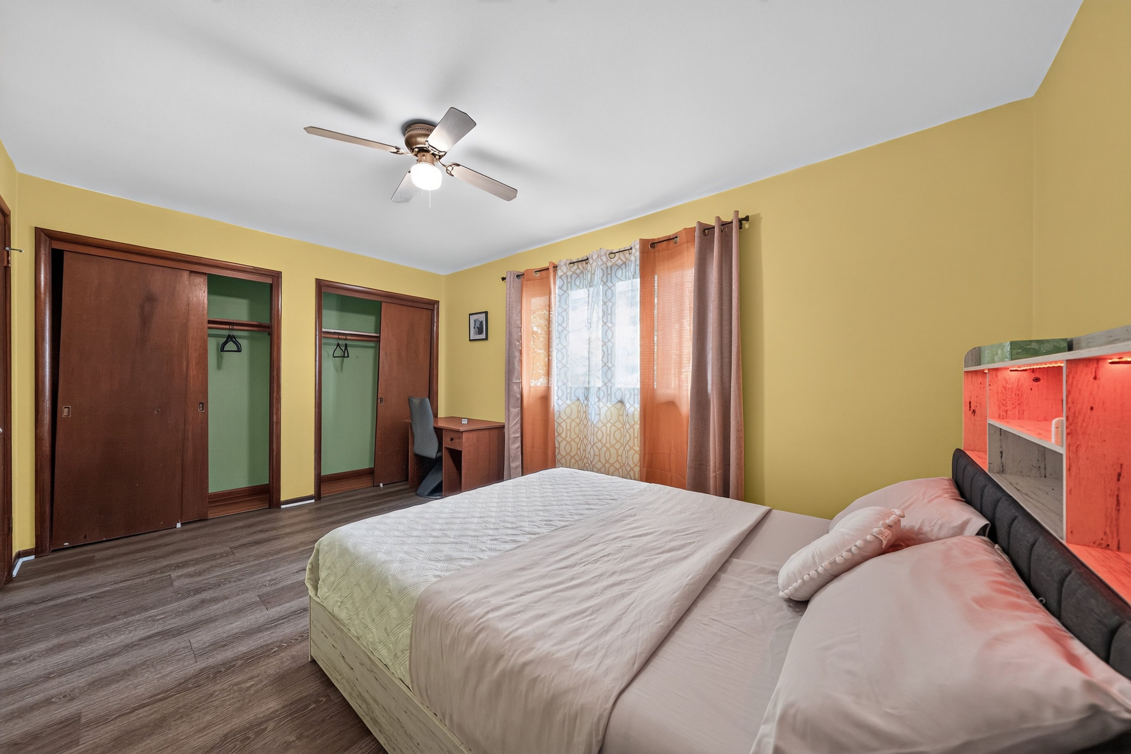 Una habitación de hotel con cama, escritorio, silla, armario y ventilador de techo.