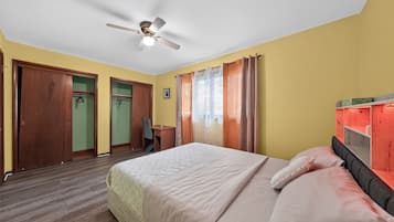 Una habitación de hotel con cama, escritorio, silla, armario y ventilador de techo.