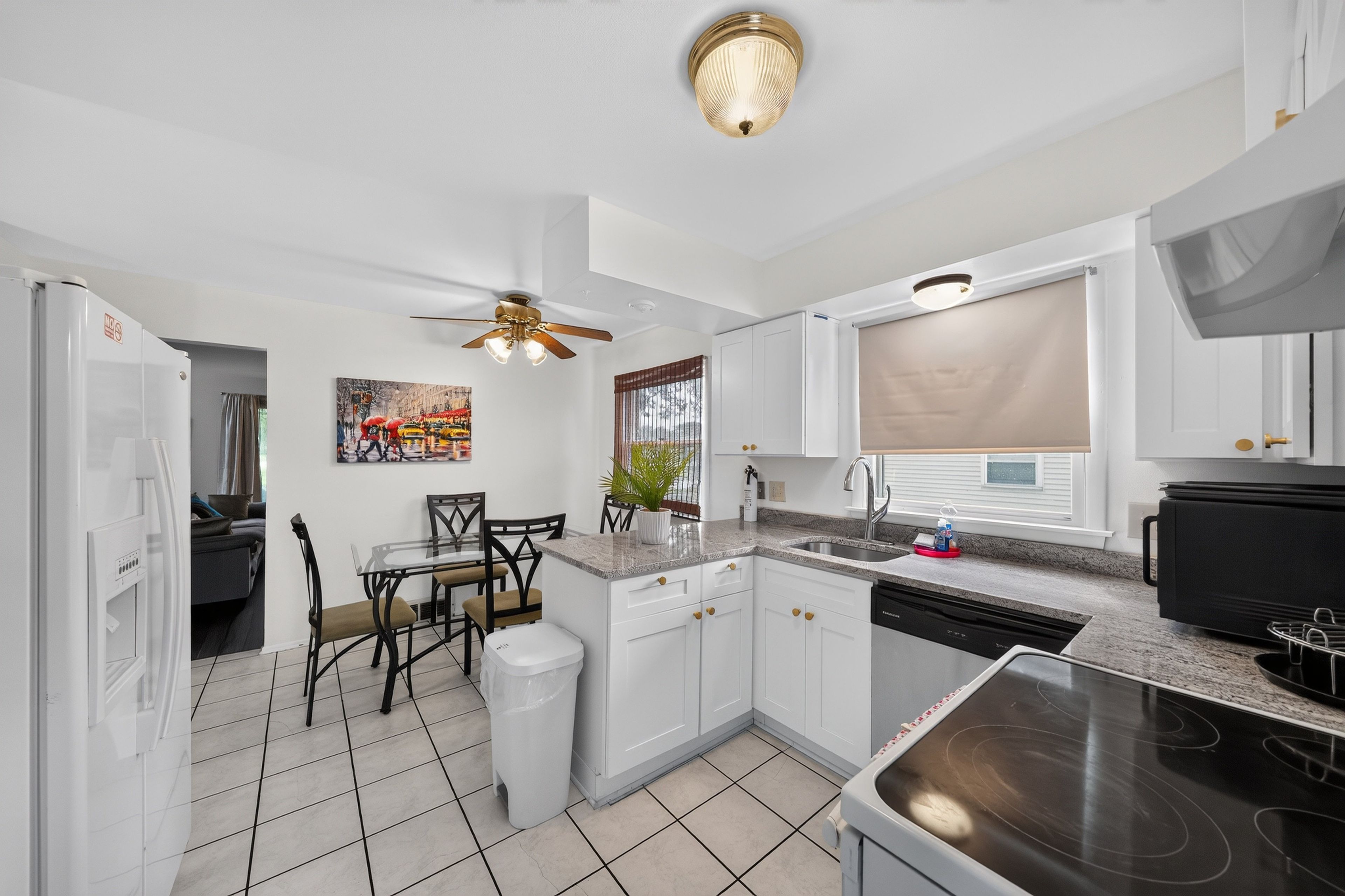 A modern kitchen with white cabinetry, a dining area with a glass table, and a ceiling fan.