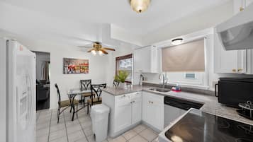A modern kitchen with white cabinetry, a dining area with a glass table, and a ceiling fan.