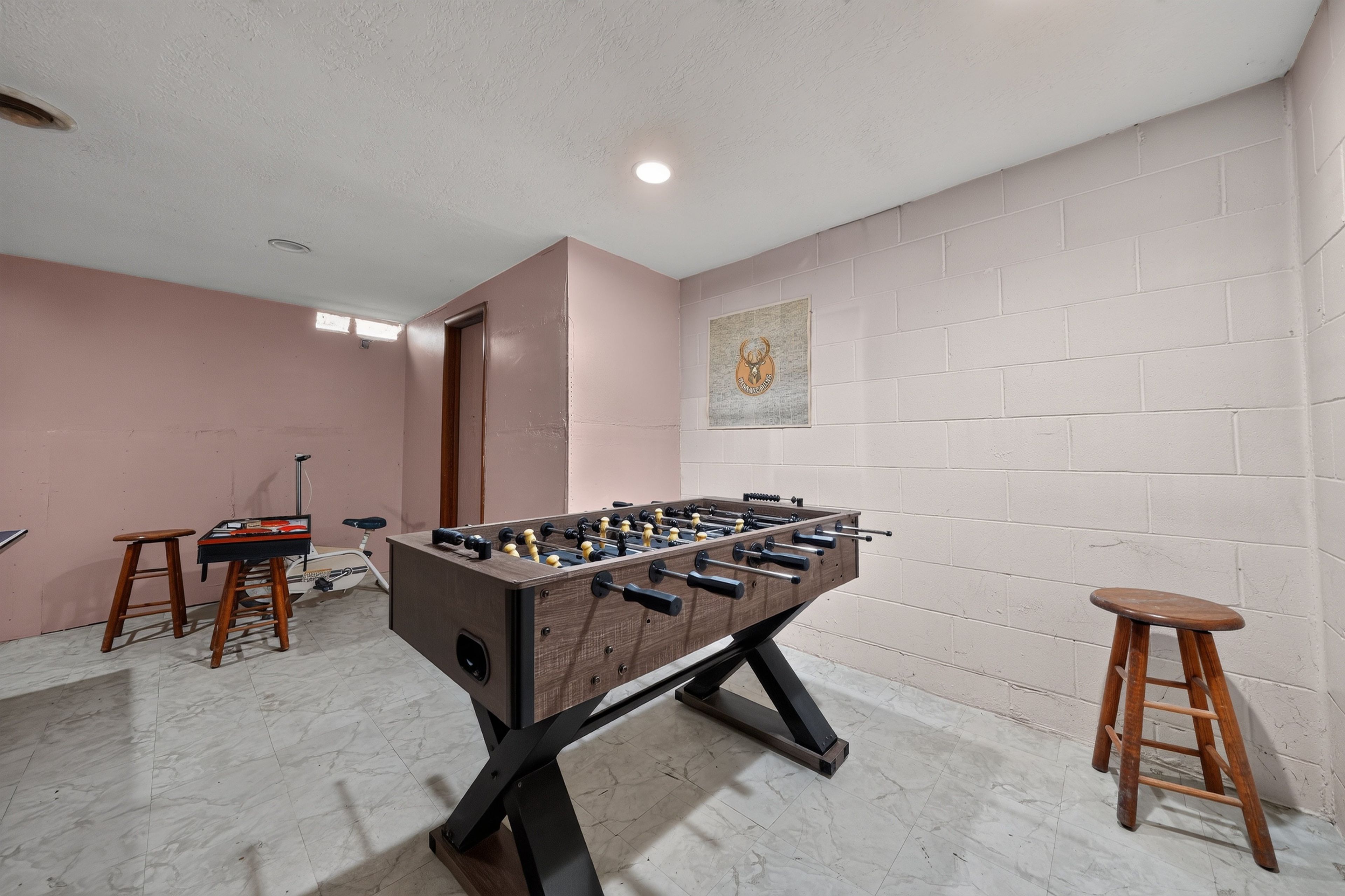 Una habitación con una mesa de futbolín, dos taburetes, un cuadro en la pared y una puerta.