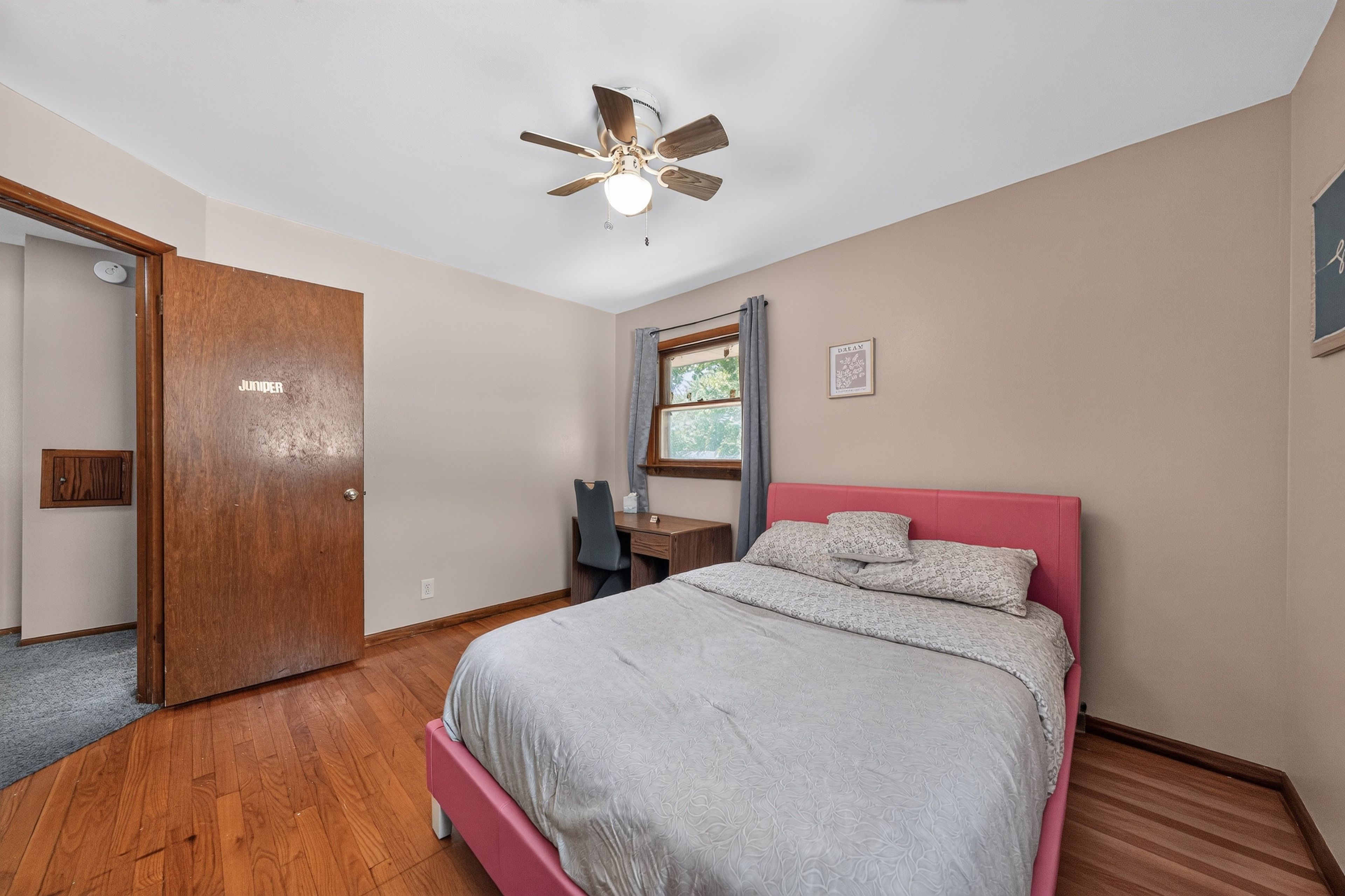 Une chambre à coucher avec un lit, un bureau, une chaise, un ventilateur de plafond et une porte.
