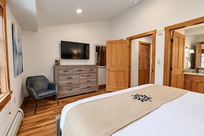 Ein Schlafzimmer mit einem Bett, einem Schminktisch, einem Sessel, einem Fernseher und Holztüren.