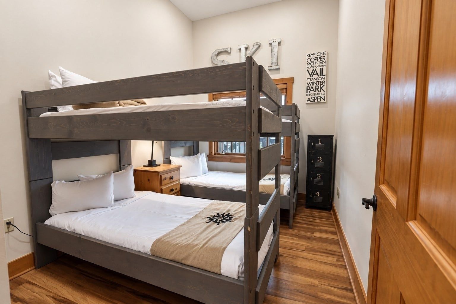 Une chambre avec un lit superposé, une tête de lit en bois, une table de chevet, une lampe et un mur orné d’une enseigne.