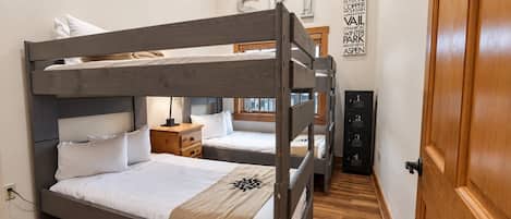 A bunk bed room with a wooden headboard, a bedside table, a lamp, and a wall with a sign.