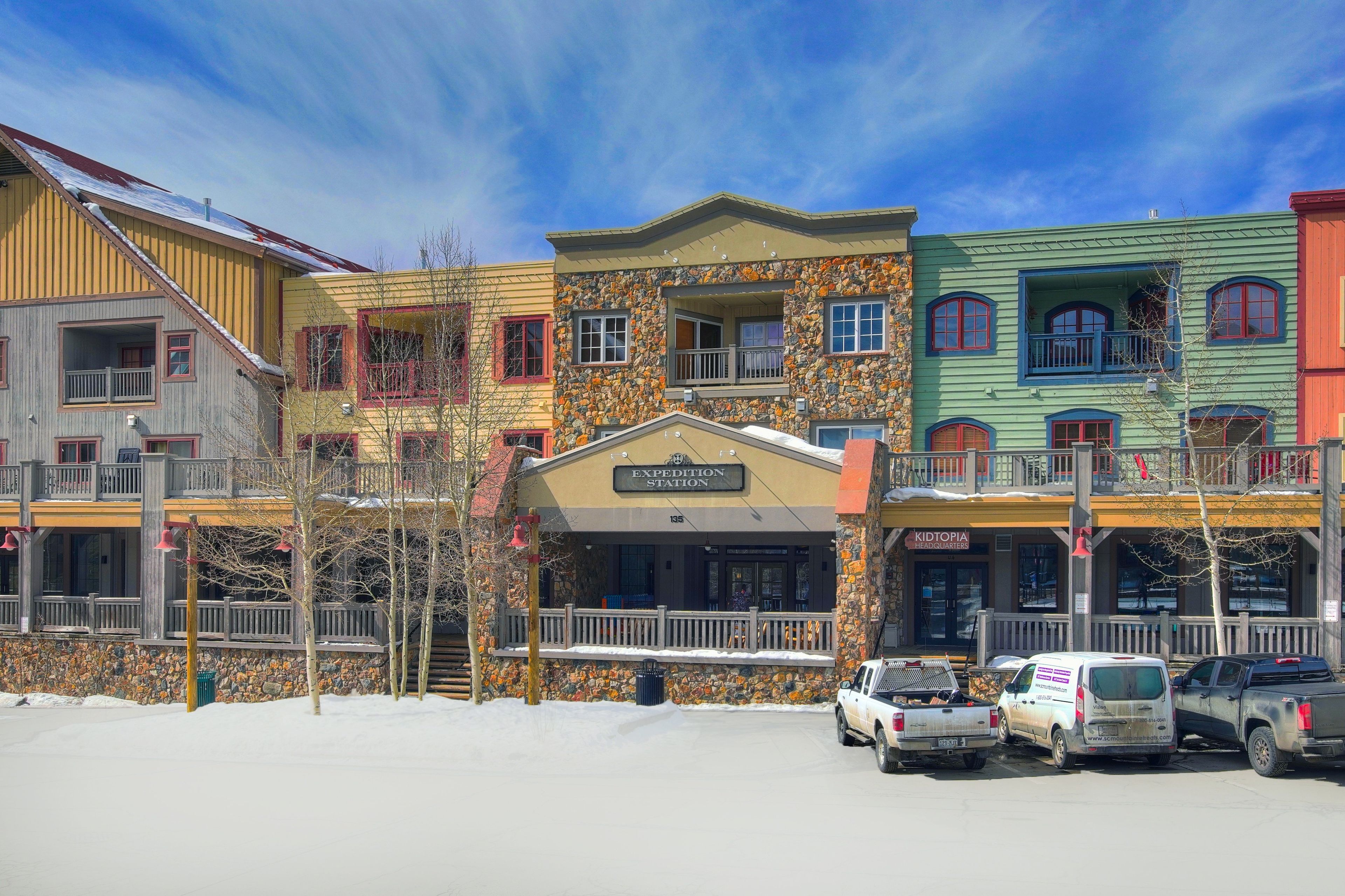 Une rangée de bâtiments colorés avec une façade en pierre, une enseigne indiquant « EXPERIENCE STATION » et une autre indiquant « KIDTOPIA HEADQUARTERS ».