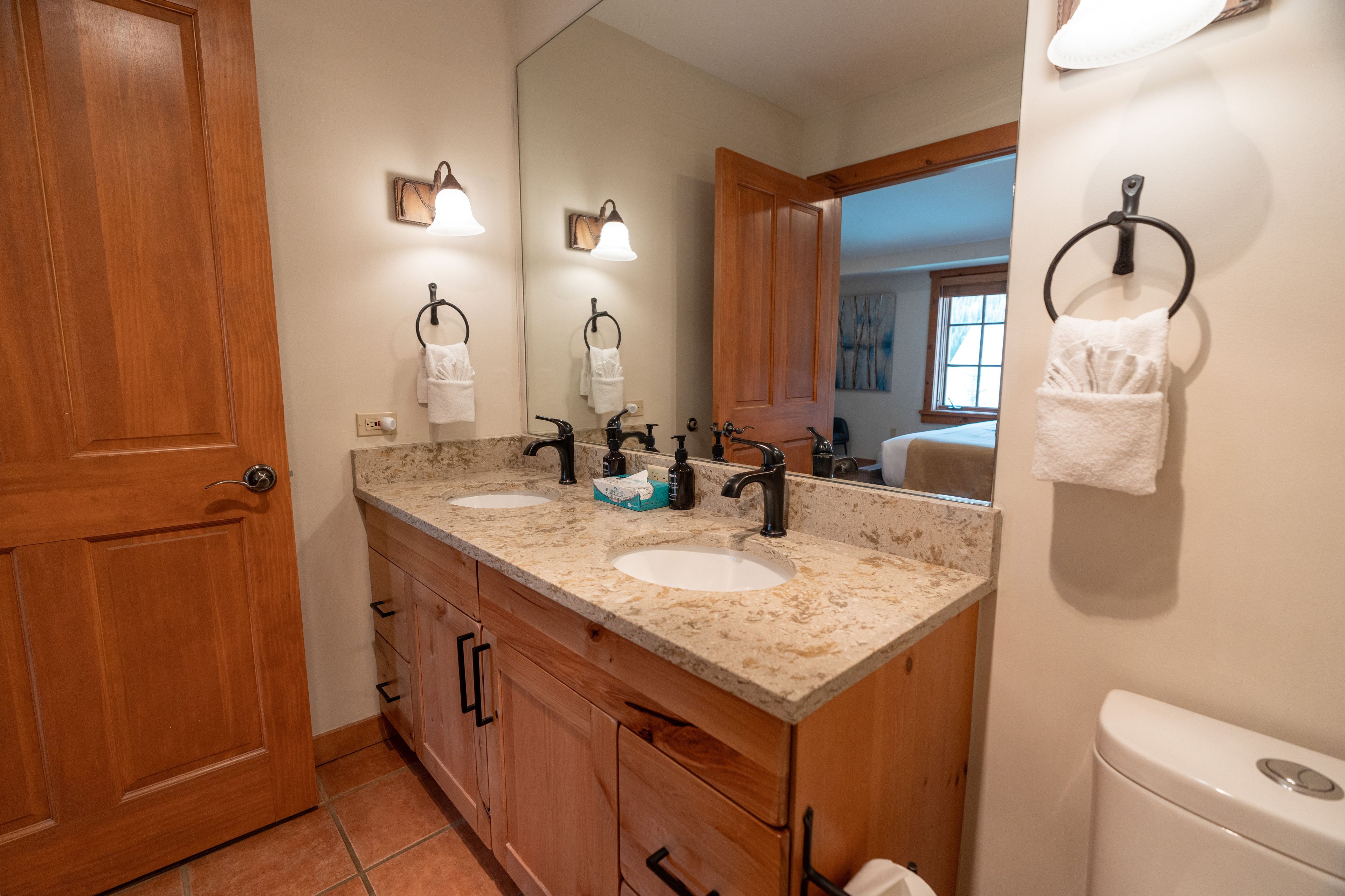 A bathroom with two sinks, wooden cabinets, a toilet, and a mirror.