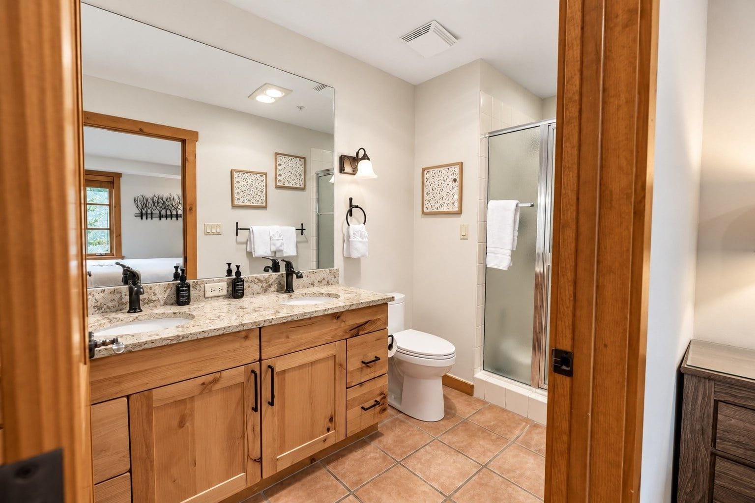 A modern bathroom with a large mirror, wooden cabinets, a white toilet, and a glass shower enclosure.