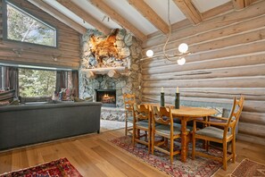 Ein Holzblockhaus-Innenraum mit Kamin aus Stein, Esstisch aus Holz und einer gemütlichen Sitzecke.