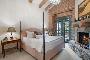 Ein Schlafzimmer in einer Blockhütte mit einem großen Bett, einem Kamin und Blick ins Freie.