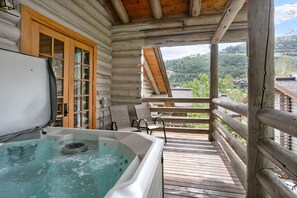 Eine Holzhütte mit Whirlpool und einem Balkon mit Blick auf eine bewaldete Landschaft.