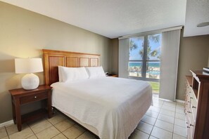 A hotel room with a large bed, a nightstand with a lamp, a view of the ocean, and a balcony with a pool. - 325 El Matador 1 Bedroom Condo (Fort Walton Beach)