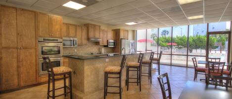 A kitchen with wooden cabinets, stainless steel appliances, a central island with bar stools, and large windows offering a view of the outdoors.