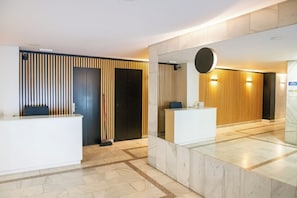 A reception area with a reception desk, a mirror, and a wall with vertical wooden slats. - Studio 4 – Fully Renovated, Modern & Centrally Located (Mad)