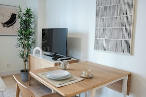 A dining area with a wooden table, a potted plant, a television, and a wall art piece. - Studio 4 – Fully Renovated, Modern & Centrally Located (Mad)