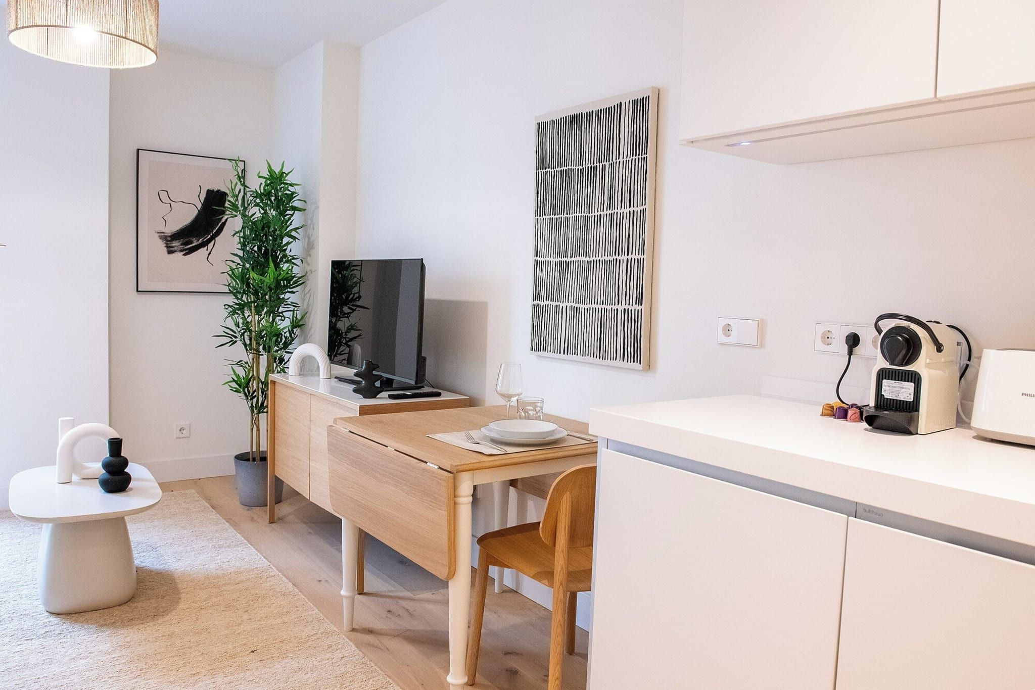 A modern kitchen with a dining table, chairs, a TV, and a coffee machine.