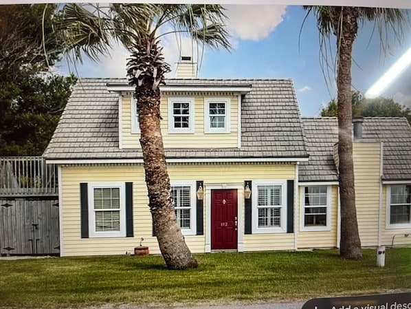 Uma casa de dois andares com porta vermelha, venezianas brancas e pequeno alpendre.