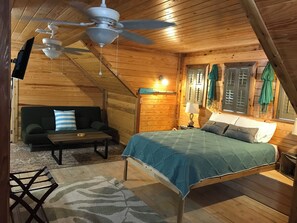Um quarto aconchegante com cama, sofá, mesa e ventilador de teto.