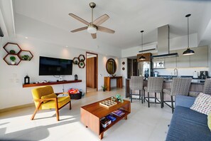 A modern living room with a flat-screen TV, a yellow armchair, a wooden coffee table, and a dining area with wicker chairs. - 2-unit Combo w/ Resort Perks < 1 Mi to Beach! (Nuevo Nayarit)