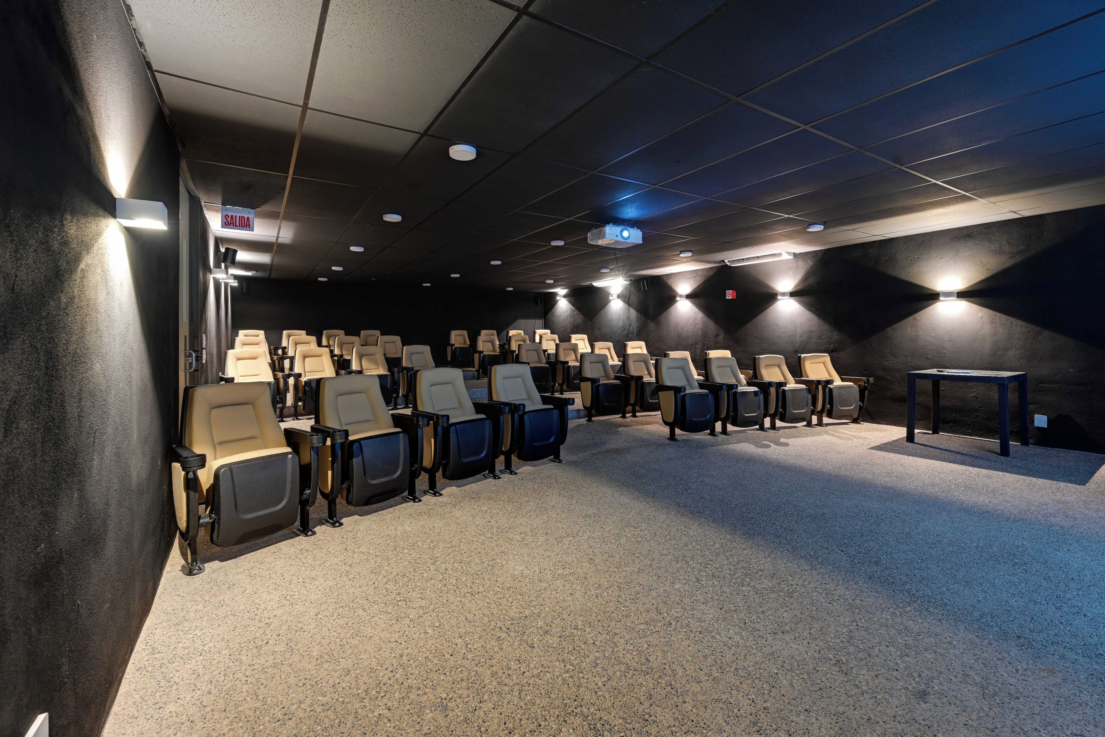A cinema room with rows of seats, a projector, and a 'SALIDA' sign.