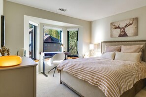 Ein Schlafzimmer mit einem großen Bett, einem Schreibtisch und einem Stuhl. Ein Fenster bietet Blick auf Bäume und ein Gebäude.