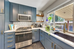 Una cocina moderna con armarios azules, electrodomésticos de acero inoxidable y un ventanal con vistas al exterior.