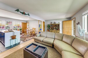 Una sala moderna con un sofá modular, un comedor con sillas, una cocina con horno empotrado y una estantería.